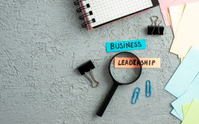 Top view of coloured envelopes and business leadership writings on magnifying glass spiral notebook on gray sand background